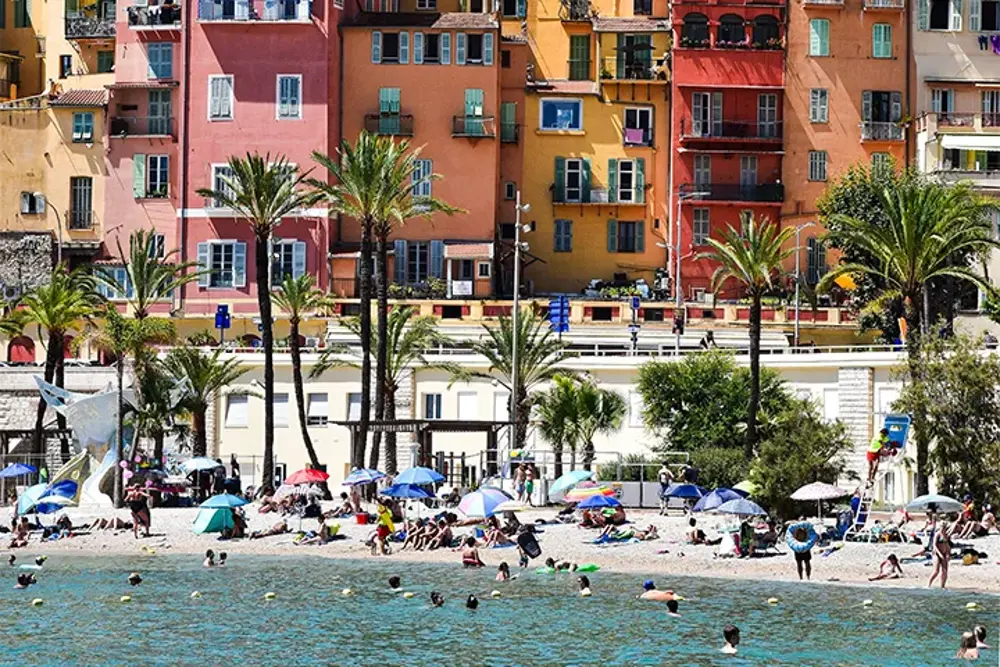 Badstrand med palmer framför färgglada fasader i rosa och gult